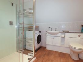 A bathroom with a shower, sink, washing machine and toilet at Lowenna Watergate Bay near Newquay