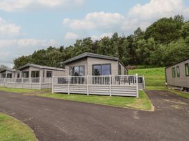 A view of cabins with decking and grass at Cedar Lodge 2 Bedrooms with hot tub in Delamere