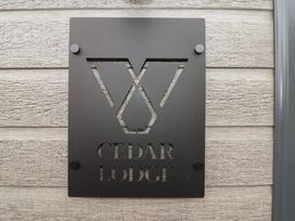A nameplate CEDAR LODGE mounted on a wooden wall at Cedar Lodge 2 Bedrooms Delamere