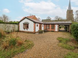 A house with a gravel driveway and a church in the background at The Pantiles in Banham