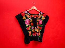 An embroidered blouse displayed on a hanger against a red background