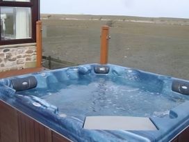 A hot tub on a deck with a stone wall at Bank House Cottage in Lancaster