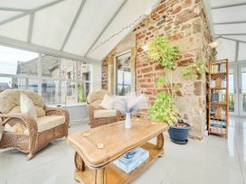 A conservatory with wicker chairs and a wooden table at Bank House Cottage in Glasson Dock