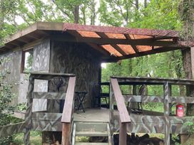 A tree house with a wooden deck and camouflage walls at The Tree House in the Woods Longhope