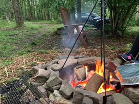 A fire pit with burning wood and a grill at The Tree House in the Woods Longhope