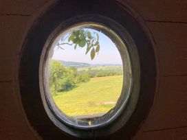 A view from a circular window overlooking a green landscape at Cosy Shepherd’s Hut in Longhope
