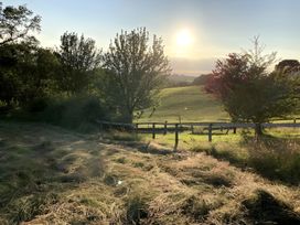 A sunset over a field with trees and a fence at Cosy Shepherd’s Hut Longhope