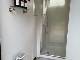 A bathroom with a shower and shelf holding toiletries at Trethowels Hidden Huts in St. Austell