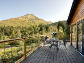 An outdoor deck with a table and chairs overlooking mountains at Pinemarten Lodge Crianlarich