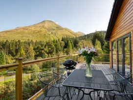 An outdoor space with a table and chairs overlooking a forest and mountain at Pinemarten Lodge Crianlarich