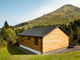 A wooden building with a deck in a mountainous area at Pinemarten Lodge Crianlarich