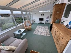 A conservatory with a sofa, armchair, coffee table, and television at Tudor Rose in Weymouth