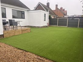 A garden with artificial grass, patio, table, chairs, and barbecue at 15 Lamsey Lane in King's Lynn