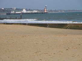 A beach with sand and a pier in the background at Woodlands House in Ringwood