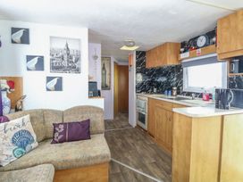 A living room with a sofa and kitchen area at Whispering Meadows - 104 Hemsby