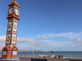 A clock tower by the ocean with benches along the pathway at Flat 7 Weymouth