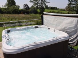 A hot tub on a deck with grass and trees in the background at Pine Lodge in Lloc near Caerwys