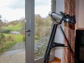A telescope by a window overlooking a garden and pond at Kerslake House Crafthole