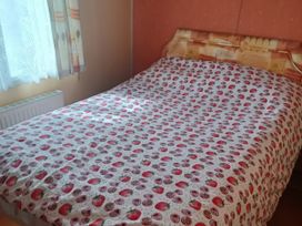 A bedroom with a bed covered in a strawberry patterned bedspread at Gannet 18 (G18) Bridlington