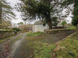 An outdoor area with a gravel path, stone wall, tree, and building at Birkbank Farm in Cockermouth