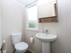A bathroom with a toilet, sink, and window at 49 Cader Idris, Hafan-Y-Mor Holiday Park in Pwllheli