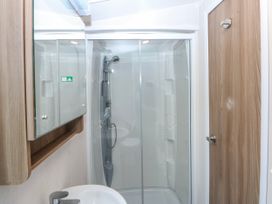 A bathroom with a shower, sink, and mirror at 49 Cader Idris, Hafan-Y-Mor Holiday Park in Pwllheli