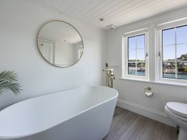 A bathroom featuring a bathtub, toilet, mirror, and windows at Bell Cottage Dartmouth