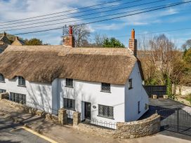 A cottage with a thatched roof and stone wall at Bridge Cottage in Chideock