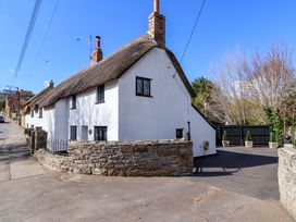 A cottage with a thatched roof and stone wall at Bridge Cottage in Chideock