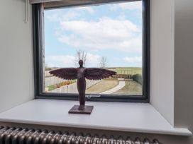 A window with a statue on the sill and a view of the outdoor pathway at The Joiners Cottage Birling near Warkworth