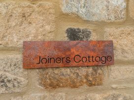 A sign reading Joiners Cottage on a stone wall at The Joiners Cottage in Birling near Warkworth