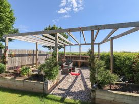 A garden with a pergola, bench, and swing at The Joiners Cottage in Birling near Warkworth
