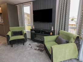 A living room with green armchairs and a television at Willow's Way in Stranraer