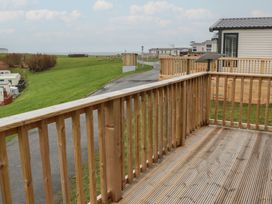 A wooden deck with railing overlooking grass and caravans at Willow's Way in Stranraer