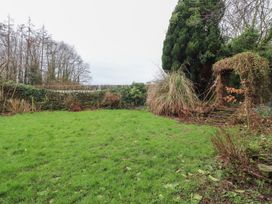 A garden with grass, trees, and a decorative archway at The Lodge House in Dolphinholme near Galgate