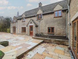 A stone house with a patio and flower bed at Manor Cottage in Carterton, Oxfordshire