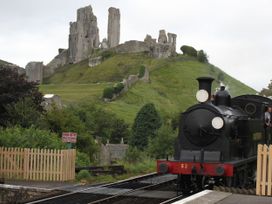 A steam train at a station with castle ruins on a hill at Swanage Bay View in Swanage