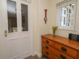 A hallway with a door, clock, window, and dresser at Kittiwake at No 20 Seahouses