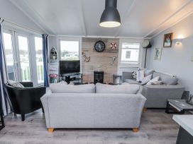 A living room with a sofa, armchair, and television at Lodge 134 in Lon Bryn Mair near Bellech
