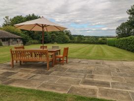 A garden with a wooden table and chairs under an umbrella at Gardeners Cottage in Chipping Norton