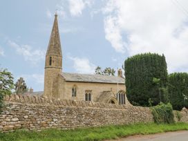 A church with a steeple and stone wall at Gardeners Cottage, Chipping Norton
