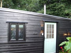 An exterior view of a black wooden lodge with a green door at Woodland Lodge The Snug Filby