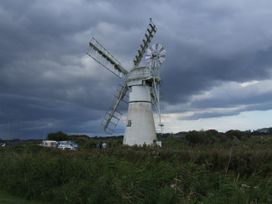 A windmill with clouds in the sky at Woodland Lodge The Snug, Filby