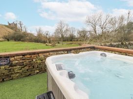 A hot tub with a stone wall and grassy area at Blue Heron Lodge in Kirkby Stephen