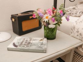 A bedside table with a radio book and flowers at The Old Studio in Penzance