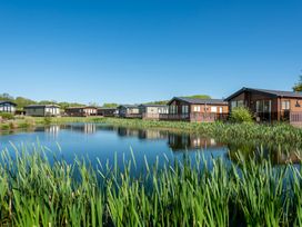 A view of lodges by a pond surrounded by greenery at Poppy in Eardisland