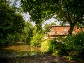 A house with a deck near a river surrounded by trees at Poppy in Eardisland