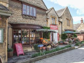 An outdoor produce display with umbrellas in front of a stone building with Broadway Deli signs at Lakeview Yurt in Beckford near Tewkesbury