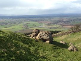 A grassy hillside with large rocks overlooking fields and farmland at Lakeview Yurt in Beckford near Tewkesbury