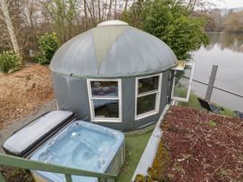 A round yurt structure with windows near a hot tub and outdoor chairs by a lake at Lakeview Yurt in Beckford near Tewkesbury